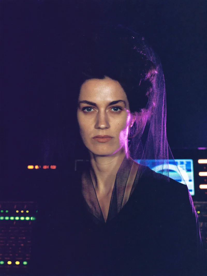 Promo photograph of Analog Widow: a pale woman with a black lace veil, lit by the glow of a mixing console